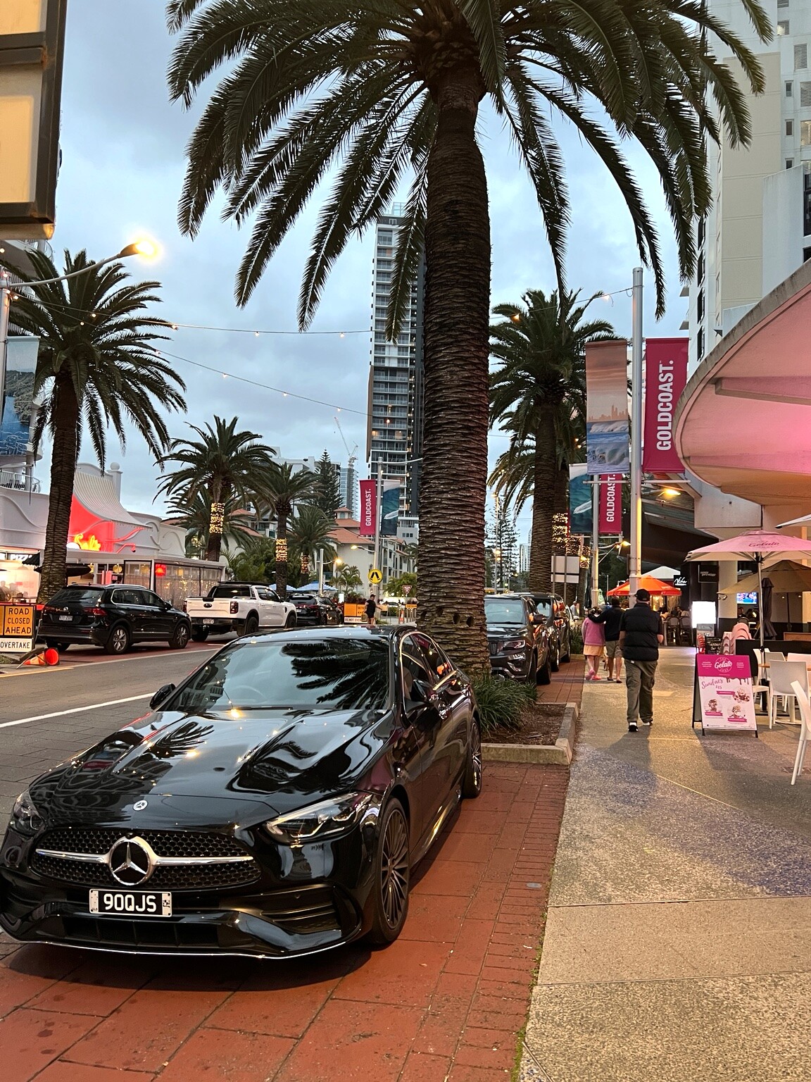 Palm-lined Broadbeach street with restaurants, pedestrians and high-rise buildings at dusk