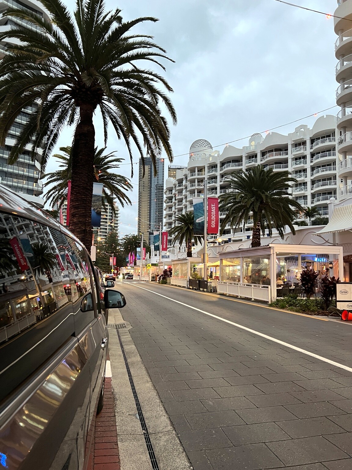 Broadbeach street with palm trees, restaurants and illuminated buildings in the evening